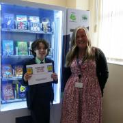 Reading competition winner Santiago Smith and Mrs McManus stand in front of the new book vending machine at Bishops' Blue Coat C of E High School.